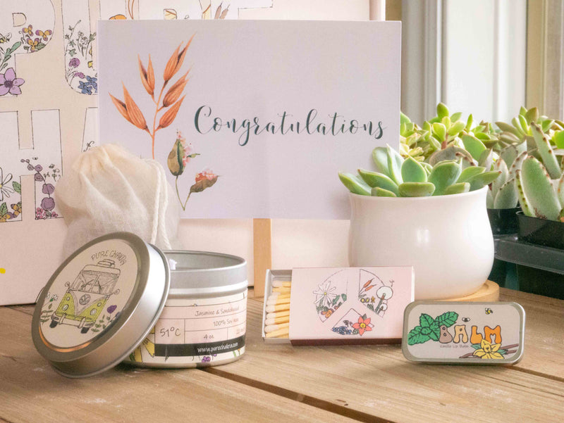 Congratulations Succulent Gift Box with candle, custom matches, lavender sachet and lip balm, in front of a decorative gift box
