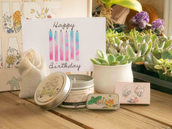 Happy Birthday Succulent Gift Box with candle, custom matches, lavender sachet and lip balm, in front of a decorative gift box