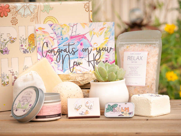 Congrats on your new home Succulent Gift Box with relax bath salt, natural soap, bath bomb, shower steamer, candle, custom matches, lavender sachet and lip balm, in front of a decorative gift box