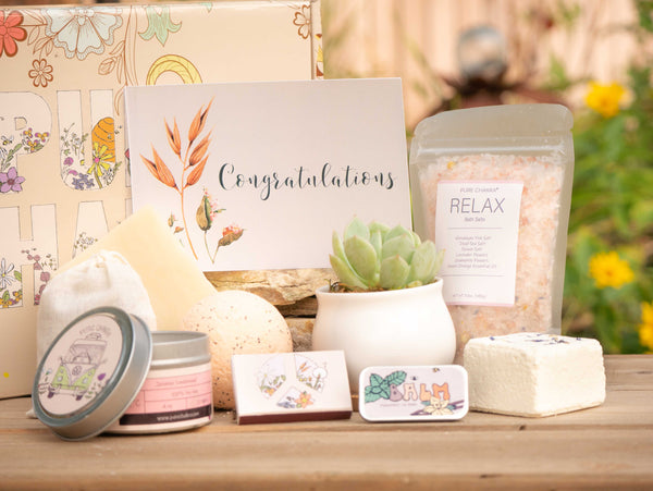 Congratulations Succulent Gift Box with relax bath salt, natural soap, bath bomb, shower steamer, candle, custom matches, lavender sachet and lip balm, in front of a decorative gift box
