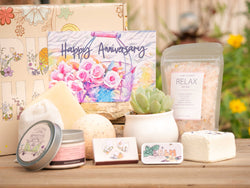 Happy Anniversary Succulent Gift Box with relax bath salt, natural soap, bath bomb, shower steamer, candle, custom matches, lavender satchet and lip balm, in front of a decorative gift box