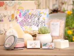 Happy Holidays Succulent Gift Box with relax bath salt, natural soap, bath bomb, shower steamer, candle, custom matches, lavender satchet and lip balm, in front of a decorative gift box