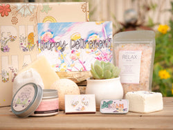 Happy Retirement Succulent Gift Box with relax bath salt, natural soap, bath bomb, shower steamer, candle, custom matches, lavender sachet and lip balm, in front of a decorative gift box