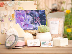 He succs Succulent Gift Box with relax bath salt, natural soap, bath bomb, shower steamer, candle, custom matches, lavender satchet and lip balm, in front of a decorative gift box