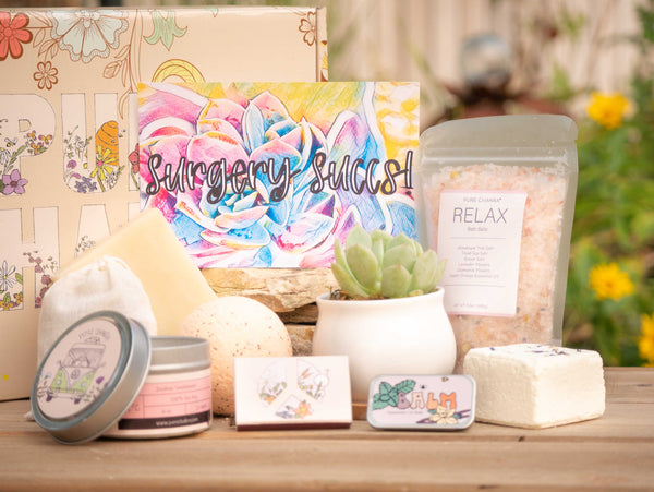 Surgery Succs Succulent Gift Box with relax bath salt, natural soap, bath bomb, shower steamer, candle, custom matches, lavender sachet and lip balm, in front of a decorative gift box