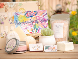 Thinking of You Succulent Gift Box with relax bath salt, natural soap, bath bomb, shower steamer, candle, custom matches, lavender satchet and lip balm, in front of a decorative gift box