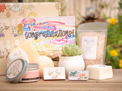 Congratulations Succulent Gift Box with relax bath salt, natural soap, bath bomb, shower steamer, candle, custom matches, lavender sachet and lip balm, in front of a decorative gift box